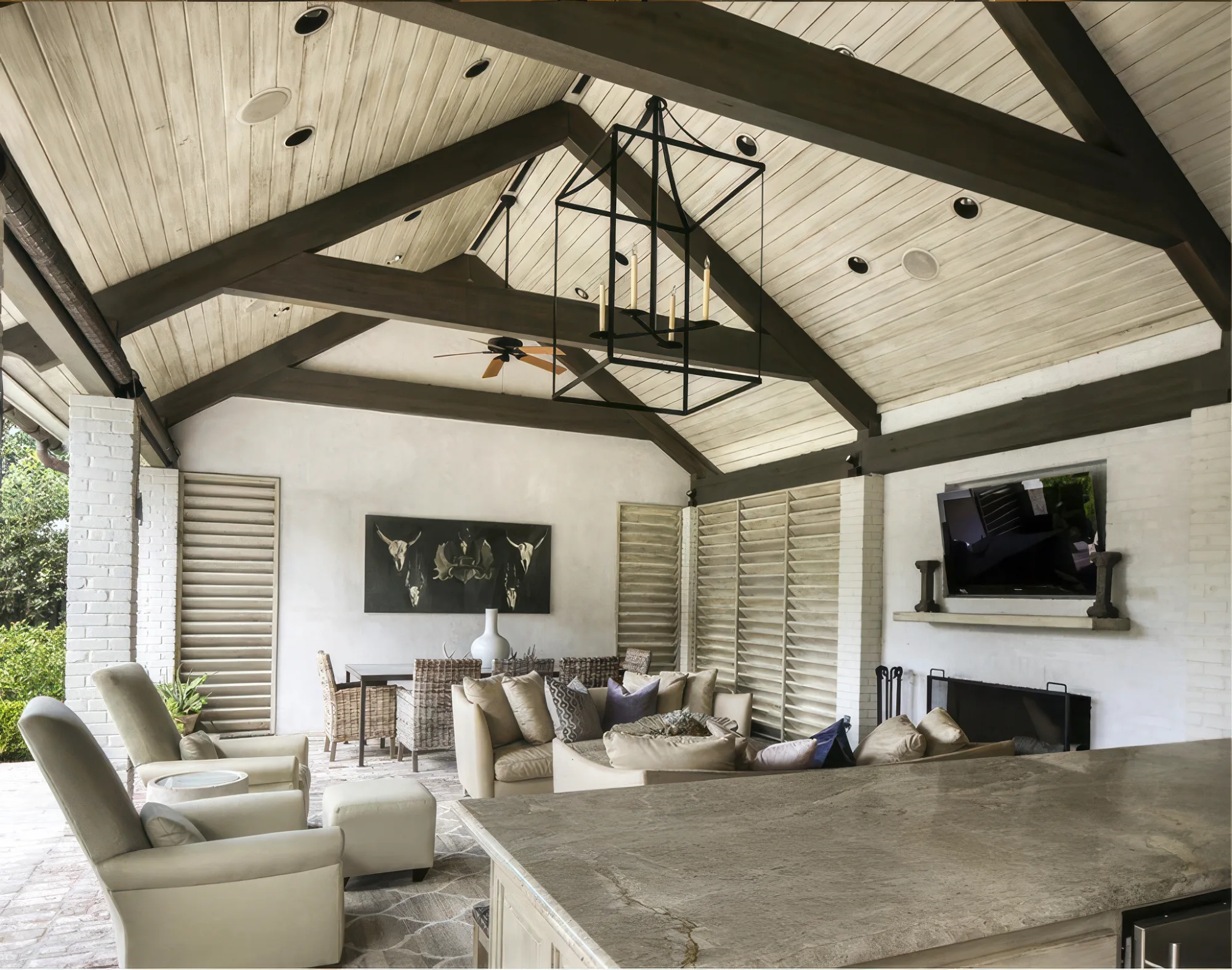 Dark timber trusses beneath a white plank ceiling over a furnished outdoor living room