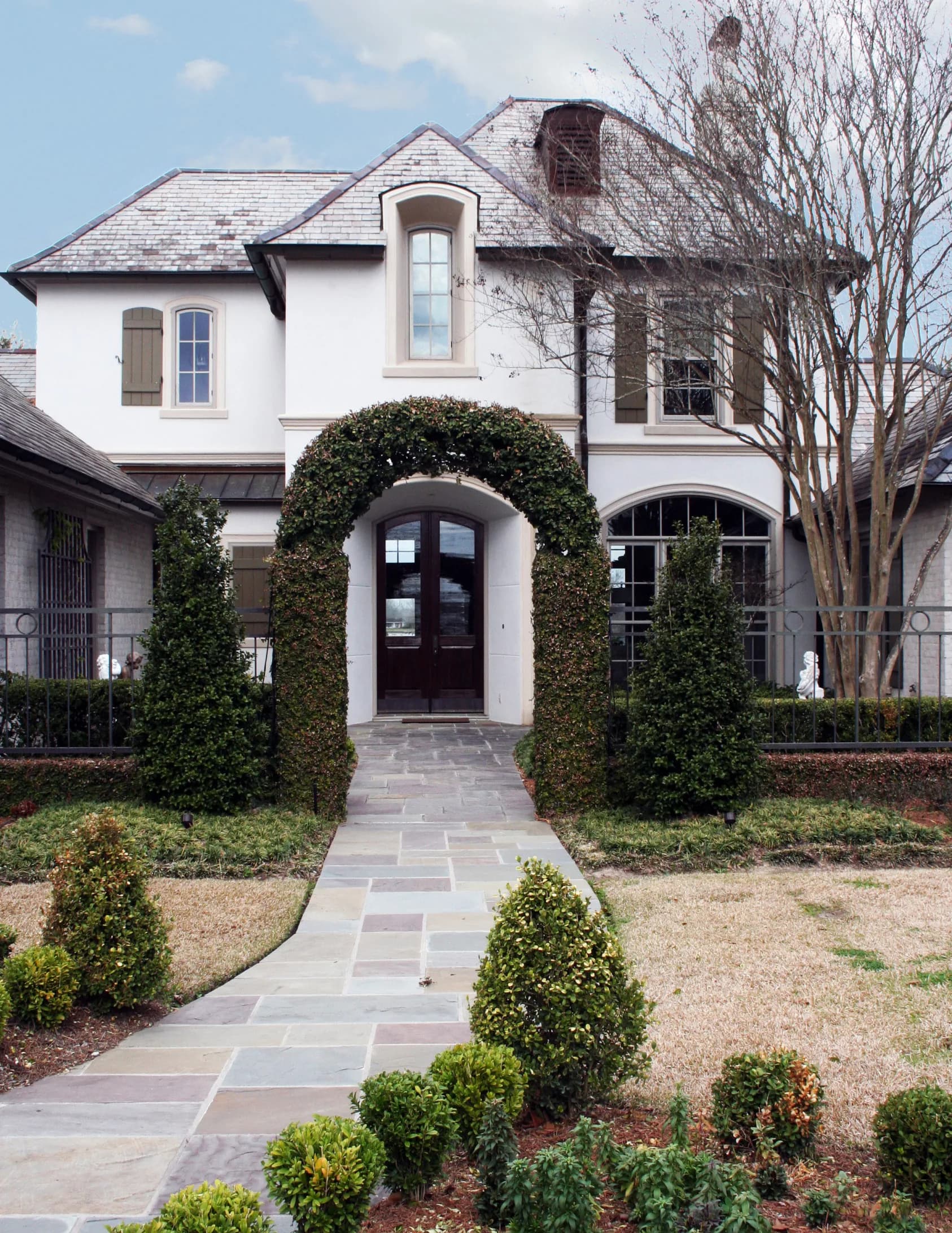 A white stucco house behind clipped hedging